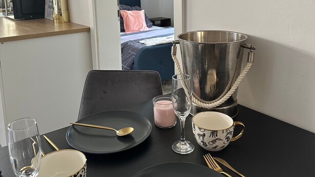 Une table à manger dressée avec des assiettes, des couverts et une bougie, avec un miroir et un seau en métal accrochés au mur.