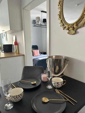 A dining table set with plates, cutlery, and a candle, with a mirror and a metal bucket on the wall.