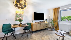 Un salon moderne comprenant un coin repas, un téléviseur à écran plat, une plante en pot et une fenêtre offrant une vue agréable.