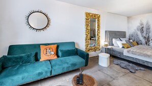 Un salon moderne avec un canapé de couleur turquoise, un miroir rond, un grand lit et une table de chevet avec une lampe.
