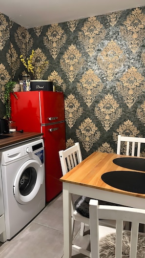 Eine kleine Küche mit einem roten Kühlschrank, einer Waschmaschine und einem Holztisch mit Stühlen.