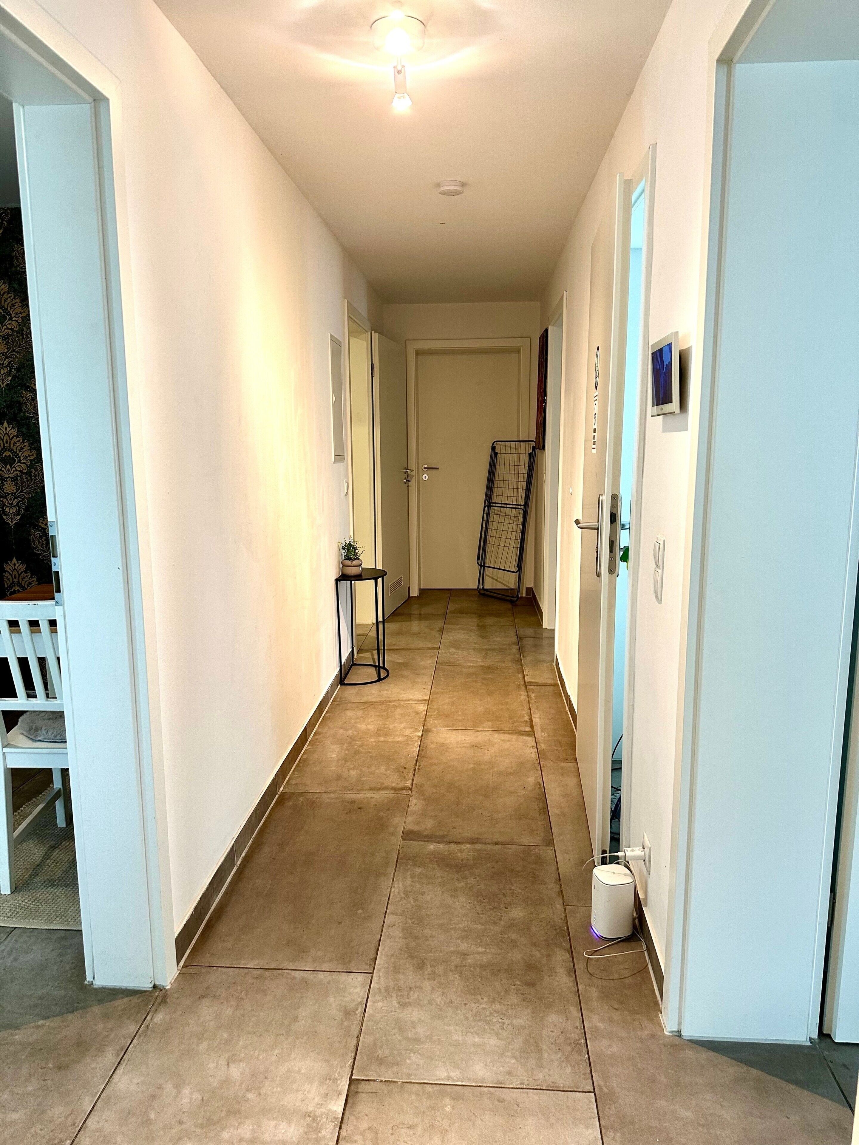 A corridor with a tiled floor, white walls, and doors leading to rooms.
