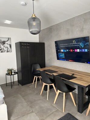 Un espace repas moderne avec une table en bois, des chaises noires, un meuble noir et un téléviseur fixé au mur qui affiche une interface utilisateur.
