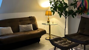 Ett mysigt vardagsrum med en brun soffa, ett soffbord i glas, en lampa och en växt.