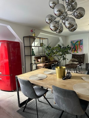 A dining area with a wooden table, black chairs, a red refrigerator, a plant, and a modern chandelier.