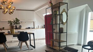 Ett modernt vardagsrum med en soffa, en matplats med stolar, ett kök i bakgrunden och ett stort fönster.
