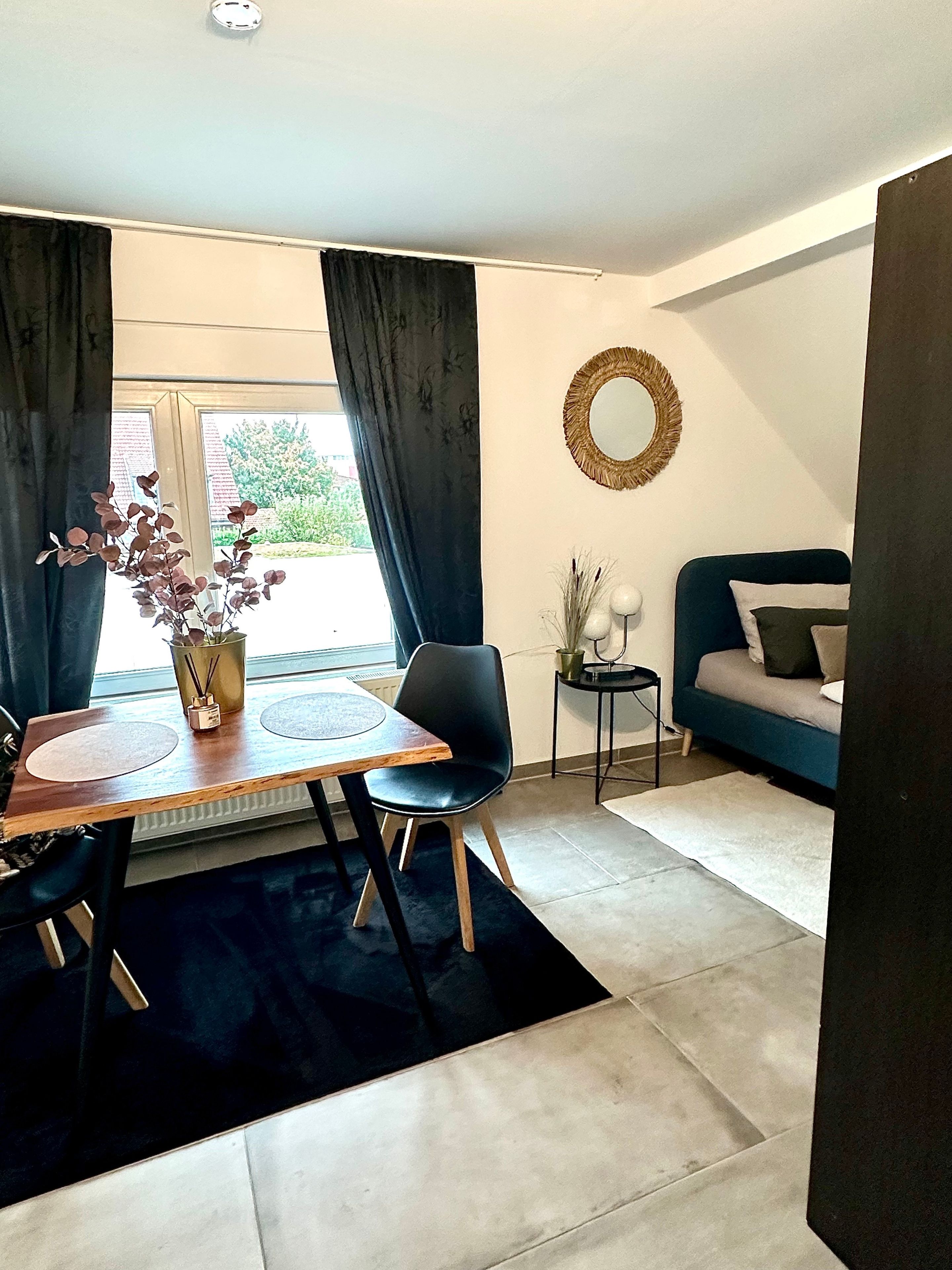 Ein modernes Wohnzimmer mit Essbereich, einem blauen Sofa, einem runden Spiegel und Blick ins Freie.
