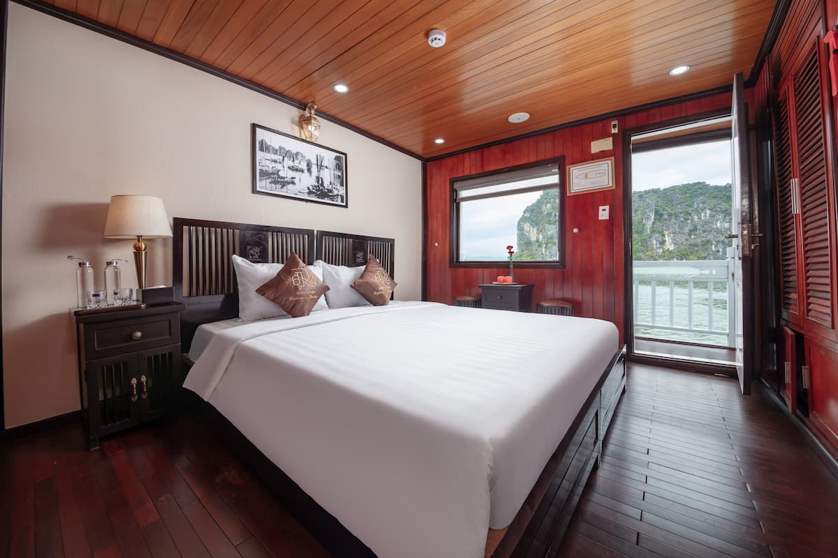 A hotel room with a large bed, wooden ceiling, and a view of a mountainous landscape through a sliding door.