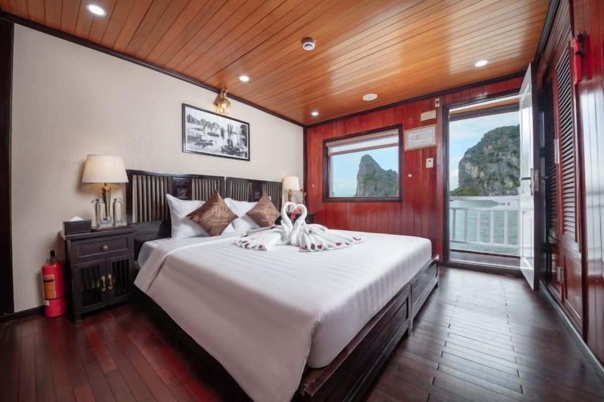 Quarto de hotel com uma cama grande, teto de madeira e varanda com vista.
