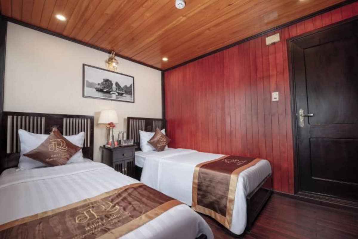 A hotel room with two beds, a wooden ceiling, a red wall, and a framed picture on the wall.