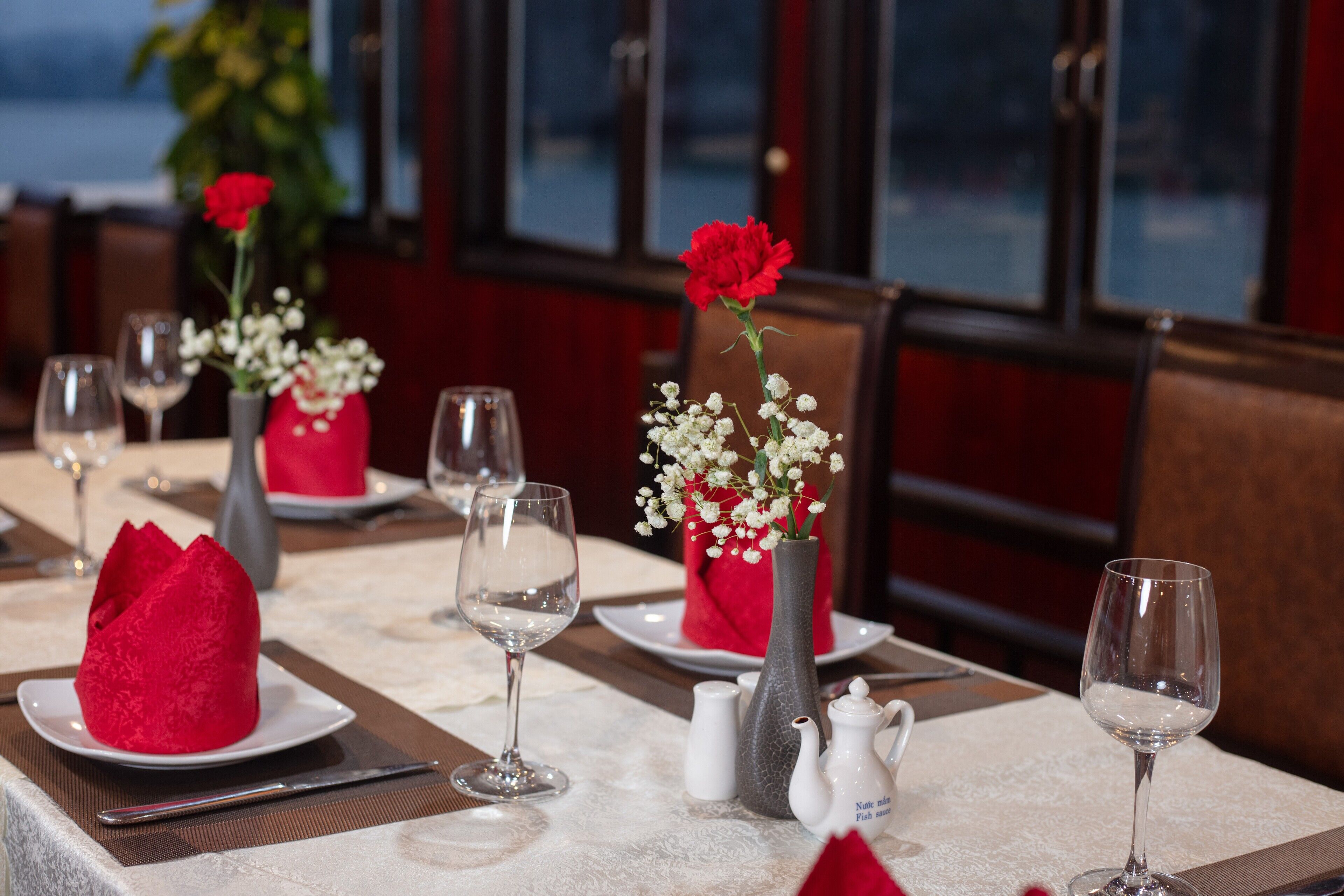 Una mesa de comedor dispuesta con servilletas rojas, copas de vino, un jarrón con flores y un salero y pimentero.