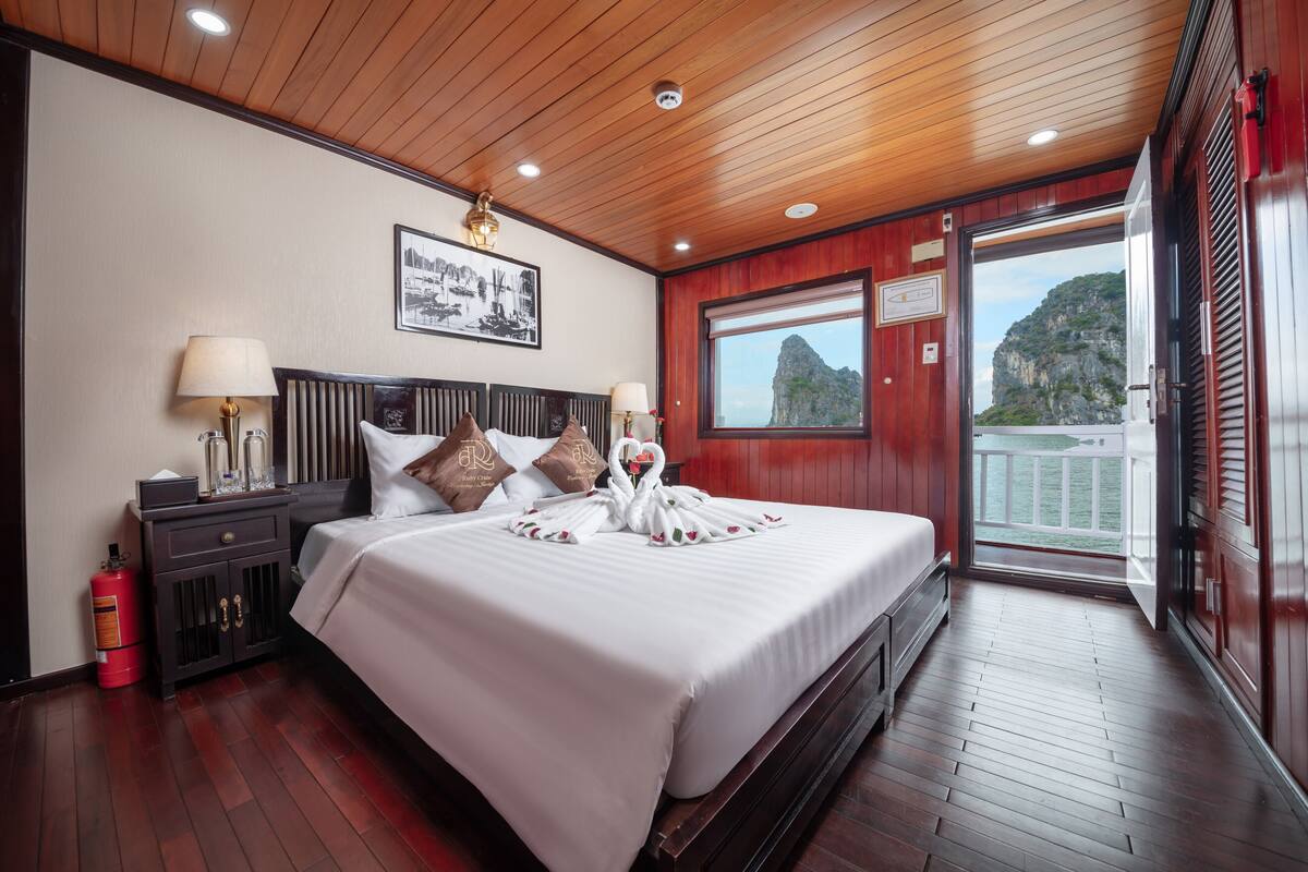 A hotel room with a large bed, wooden ceiling, and a balcony with a view of cliffs.