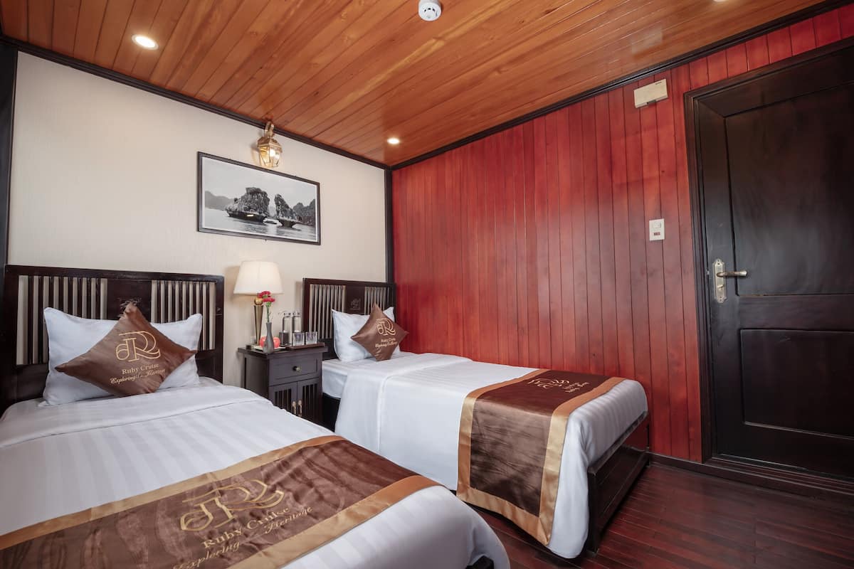 A hotel room with two beds, wooden ceiling, a framed picture on the wall, and a dark door.