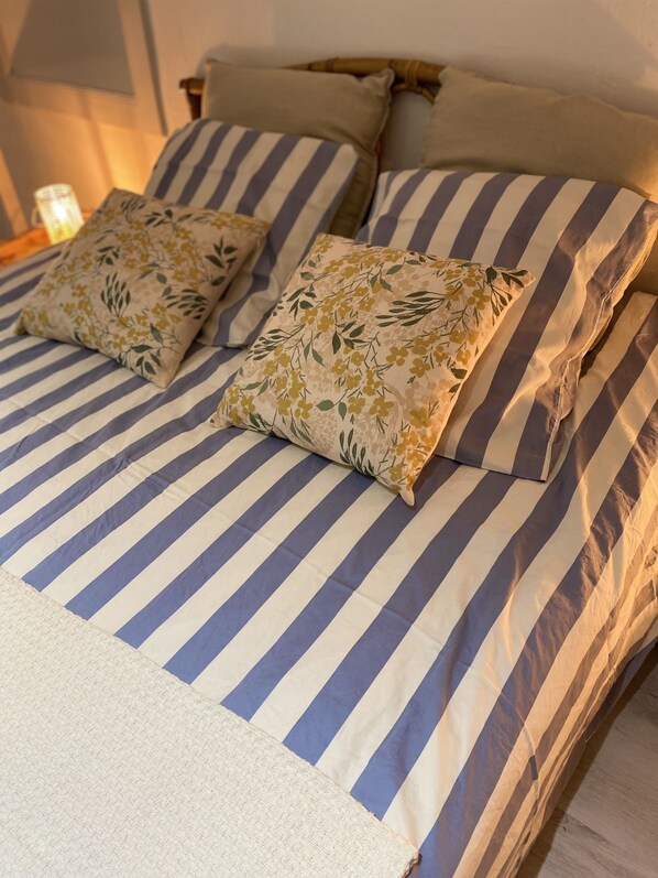 A bed with striped bedding and floral pillows. - La Petite Maison de Coline (Reville)