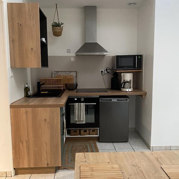 Une cuisine compacte avec des meubles en bois, un four encastré, un lave-vaisselle, un four à micro-ondes et une plante suspendue.