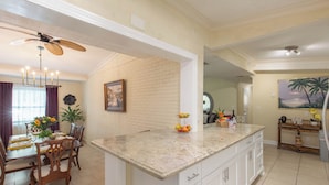 Una cocina amplia con una isla grande, muebles blancos y un comedor con mesa y sillas de madera.