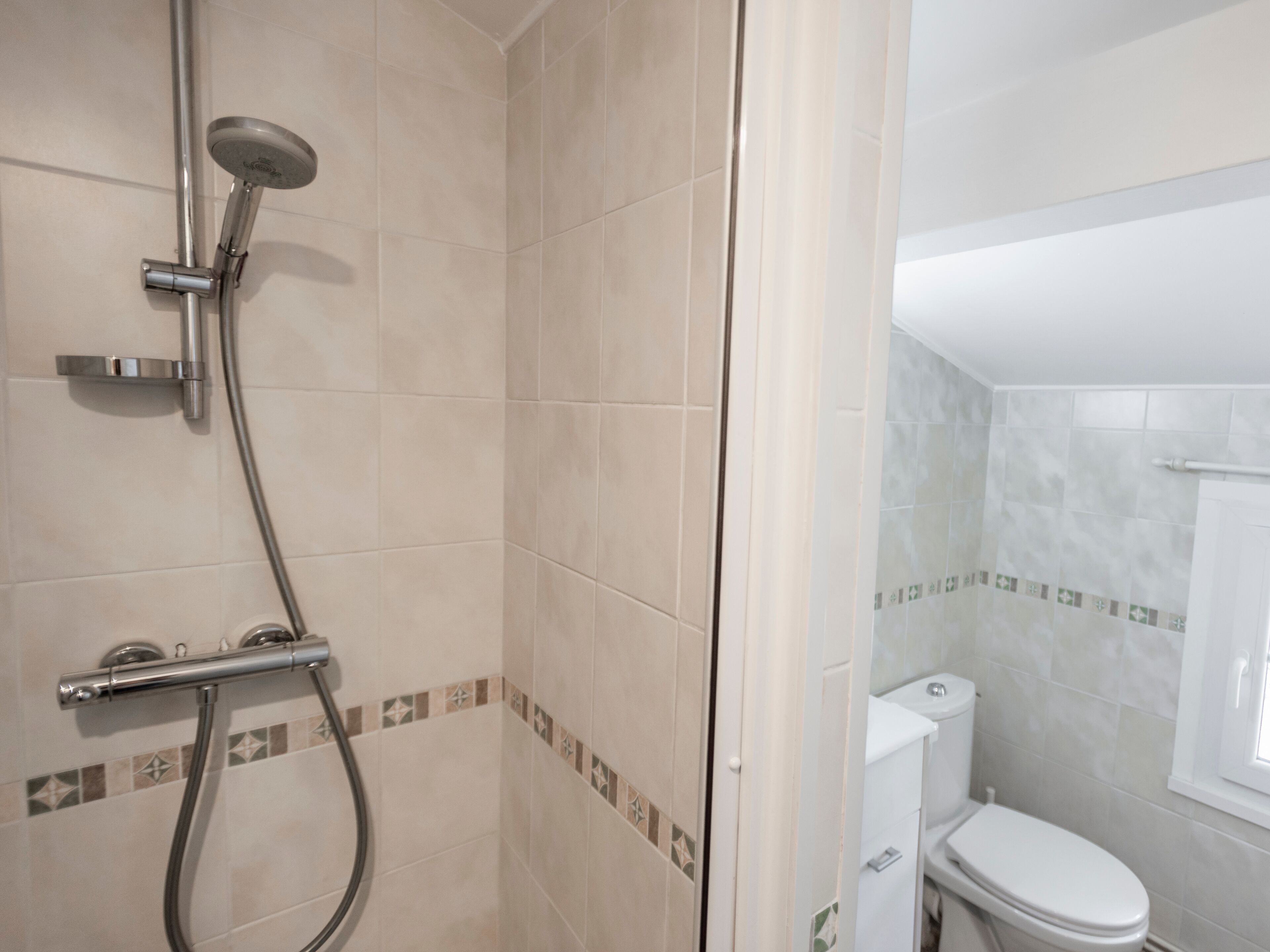 A bathroom with a shower, toilet, and a tiled floor.