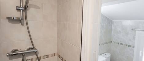 A bathroom with a shower, toilet, and a tiled floor.
