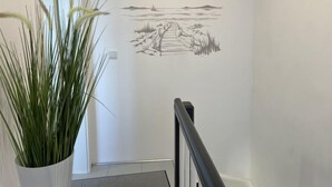 Un pasillo con un mural que muestra un paisaje con un sendero que lleva a una masa de agua y formas de terreno lejano.