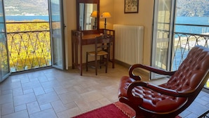Quarto com escrivaninha, cadeira e vista para um corpo de água e montanhas.
