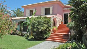 Une villa rose ornée d’une arche en pierre, d’un escalier rouge et d’un jardin bien entretenu.