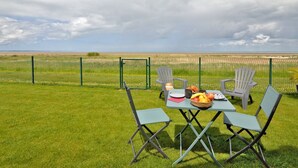 An outdoor dining area with a table and chairs, a basket of fruit, and a view of the beach and sea in the background. - l'atelier des rêves by Interhome (Cherrueix)