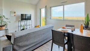 A modern living room with a sofa, dining table, chairs, a TV, and a large window offering a view of the countryside. - l'atelier des rêves by Interhome (Cherrueix)