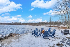 A lakeside setting with a fire pit and Adirondack chairs.
