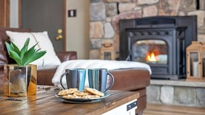 Ein gemütliches Wohnzimmer mit Kamin aus Stein, einem Holztisch mit Keksen und einer Topfpflanze.