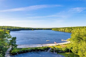A lake surrounded by lush greenery, a parking area, and a small dock with an American flag. - Lakefront, Hot Tub, Dog Friendly, Resort Amenities (Gouldsboro)