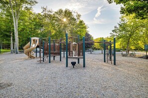 A playground with a slide and climbing structures, surrounded by trees and a gravel surface. - Lakefront, Hot Tub, Dog Friendly, Resort Amenities (Gouldsboro)