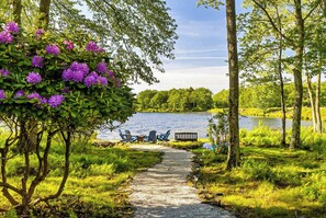 Un sendero de grava que conduce a una zona junto al lago, con sillas y un banco.