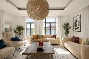 A spacious living room with a large window, a central coffee table, and a modern chandelier.