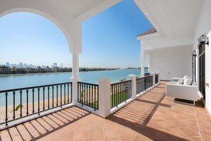 A balcony with a view of a river and city skyline, white furniture, and a tiled floor.