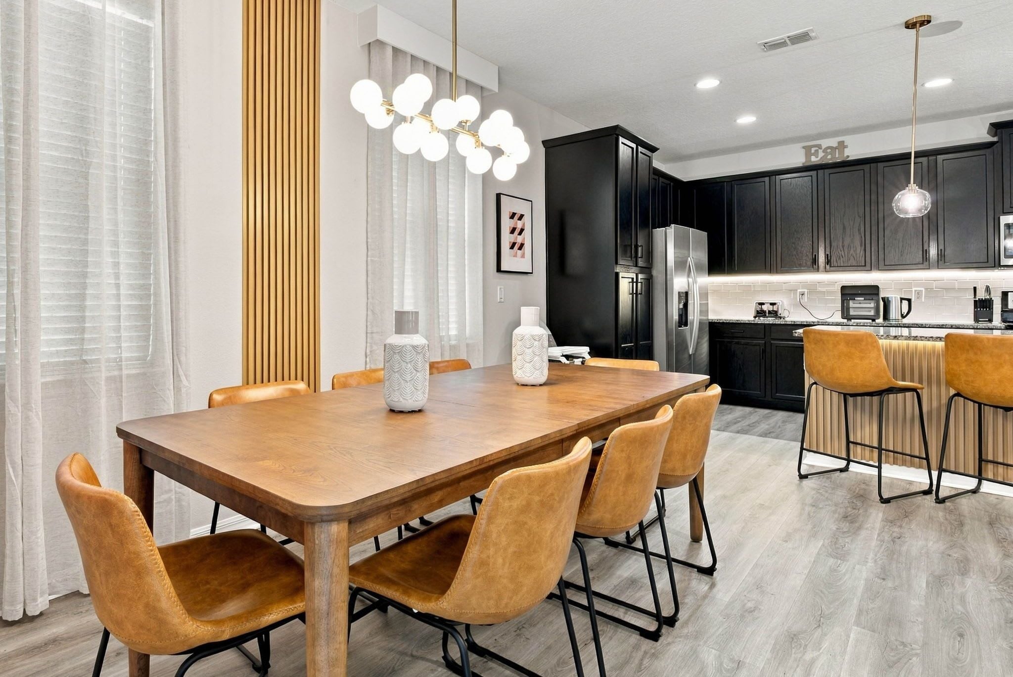 A modern kitchen with dark cabinets, a stainless steel refrigerator, and a bar area with stools.