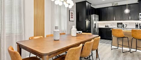 A modern kitchen with dark cabinets, a stainless steel refrigerator, and a bar area with stools.