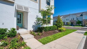 A two-story residential building with a front entrance, a small porch, and a landscaped garden with shrubs and a tree. - Private Pool Oasis, Solara Resort,  Stylish Decor (Kissimmee)