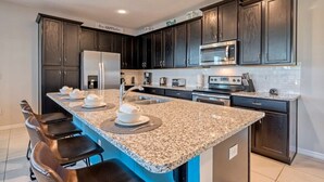 A modern kitchen with dark wood cabinets, granite countertops, stainless steel appliances, and a breakfast bar with seating. - Private Pool Oasis, Solara Resort,  Stylish Decor (Kissimmee)