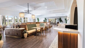 A spacious hotel lobby with a reception desk, seating area, and large windows offering views of the outdoors.