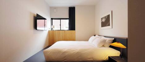 Un dormitorio con cama, mesita de noche, lámpara, ventana y una obra de arte en la pared.