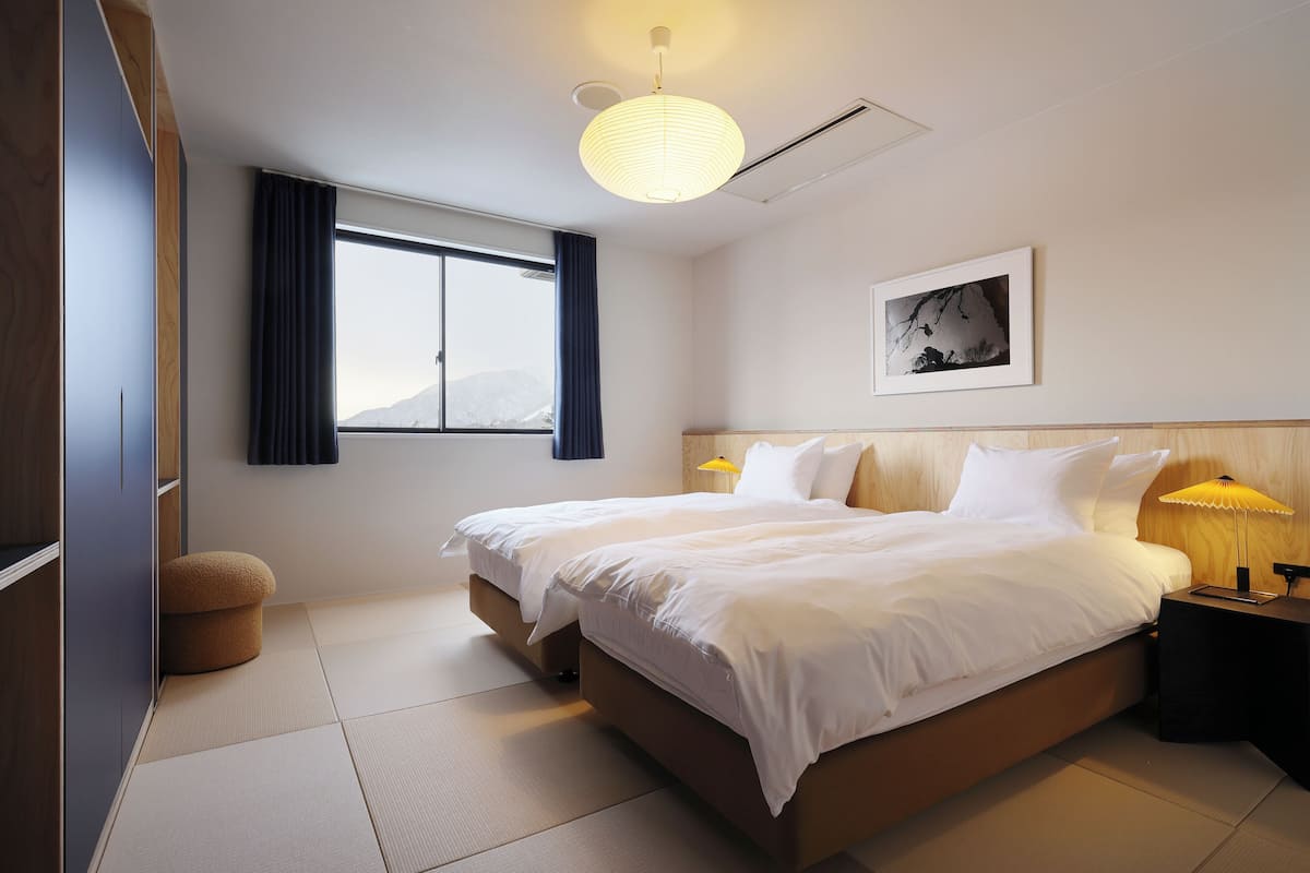 Un cuarto de hotel con una cama grande, una mesita de noche con una lámpara, una ventana con cortinas y un cuadro en la pared.