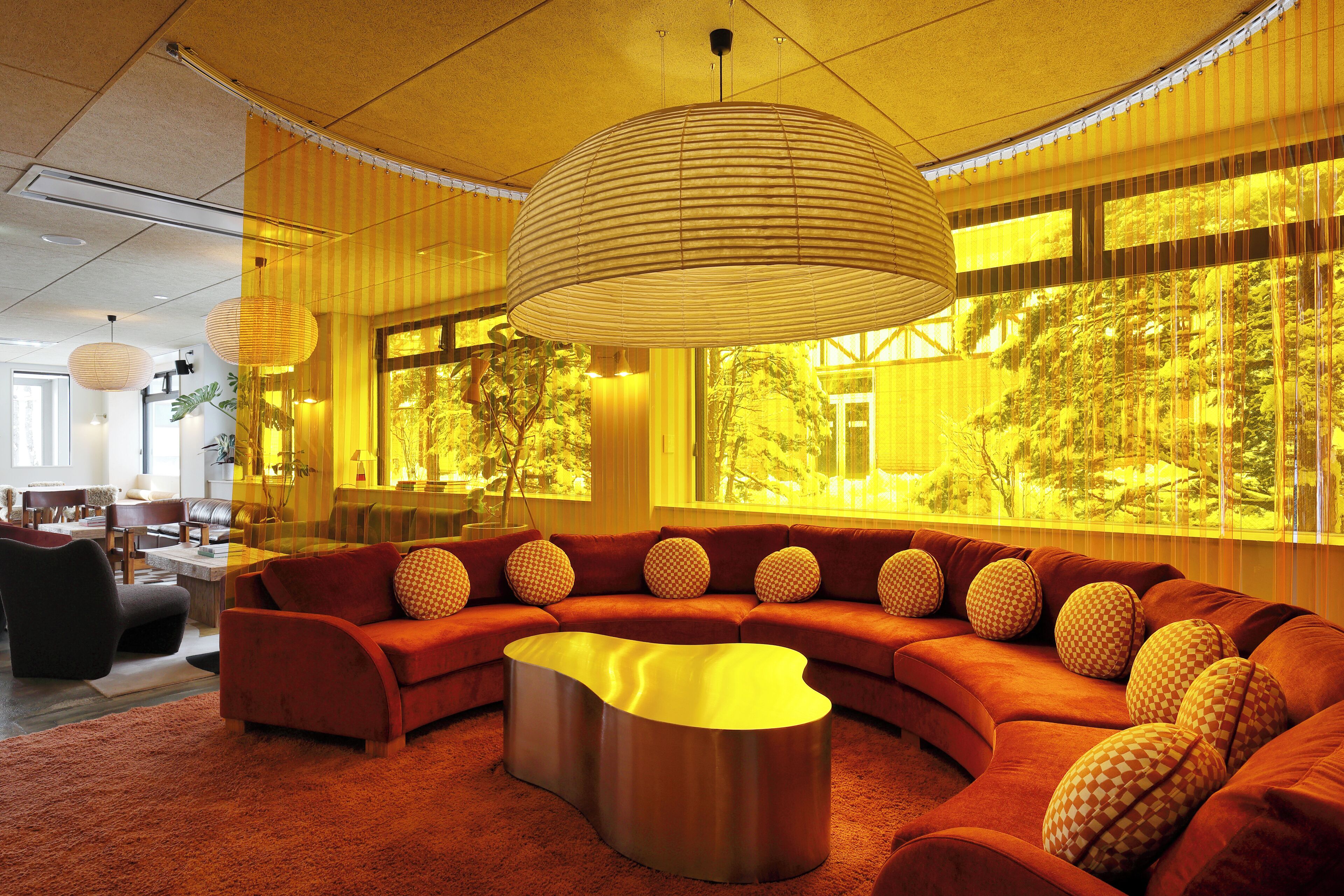 A modern living room with a curved sofa, a metallic coffee table, and a large window with a view of trees.