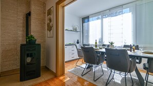 A modern dining area with a wooden floor, a dining table set with chairs, a kitchen area with white cabinets, and a large window with blinds. - Awesome apartment in Okrug Gornji with WiFi (Okrug Gornji)