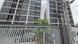A multi-story residential building with a gated entrance, a parked car, and visible balconies.