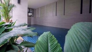 A spacious indoor area with a concrete floor, large green plants, and a wall with vertical black lines.