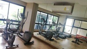 A gym with various exercise machines, large windows, and an air conditioning unit.