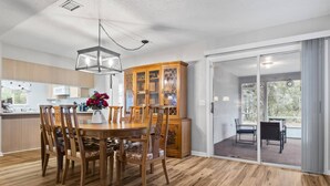 A modern kitchen with wooden cabinets, a dining area with a wooden table and chairs, and a sliding glass door leading to an outdoor patio.