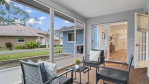 A balcony with wicker chairs and a small table, overlooking a residential area with houses and a lawn.