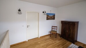 Een kamer met een houten vloer, een witte deur, een stoel, een kast en twee wandlampen.