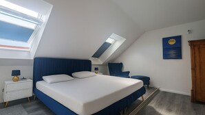 Een slaapkamer met een groot bed, dakraam, nachtkastje, stoel en een schilderij aan de muur.